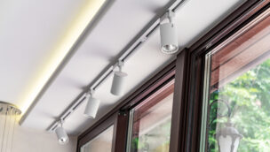 Ceiling-mounted track lighting with white cylindrical fixtures alongside large windows overlooking greenery.