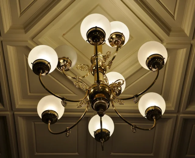 An ornate brass chandelier with eight frosted glass globes is mounted on a coffered ceiling.