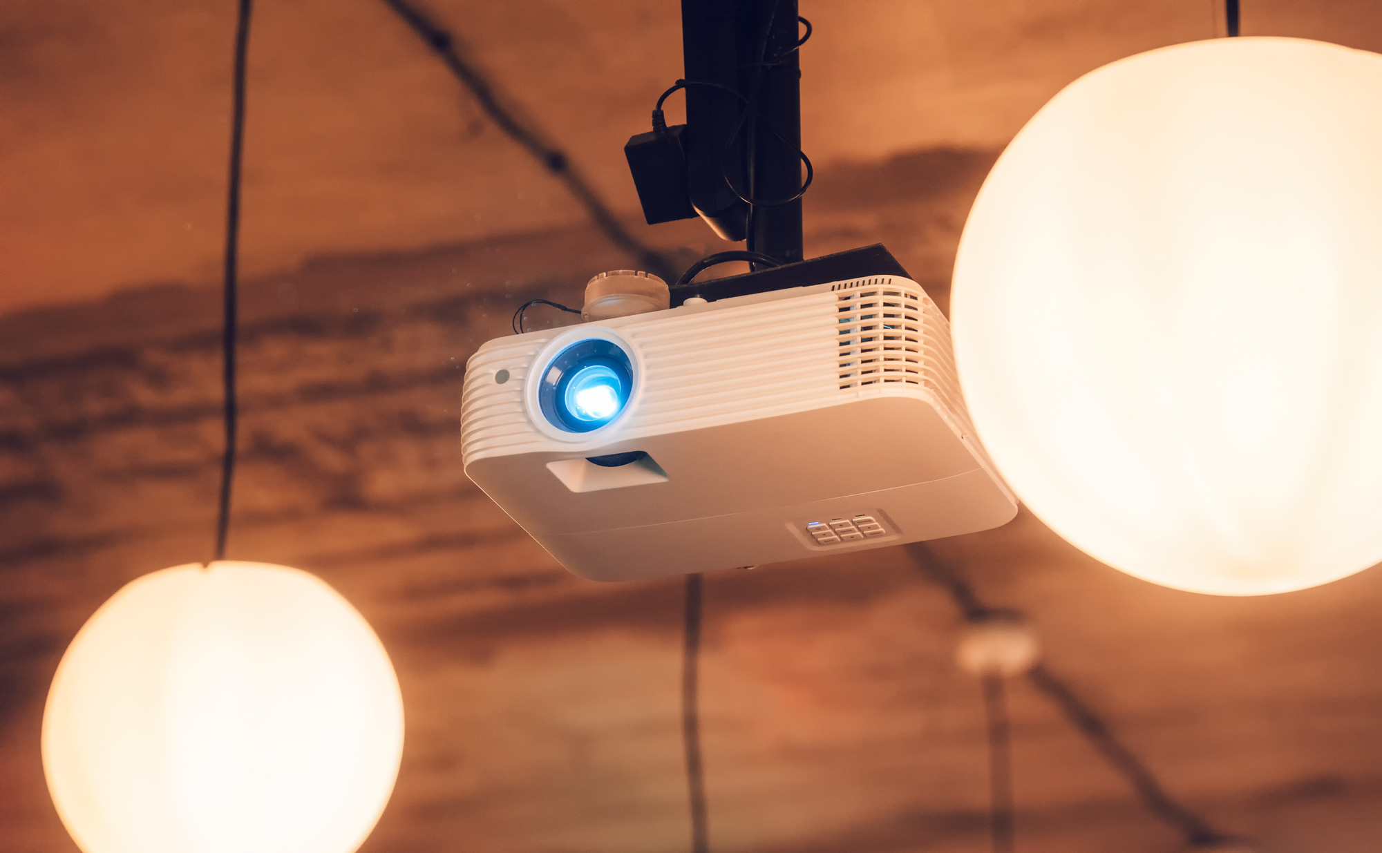 Ceiling-mounted projector with a blue light beam, surrounded by two round pendant lights.