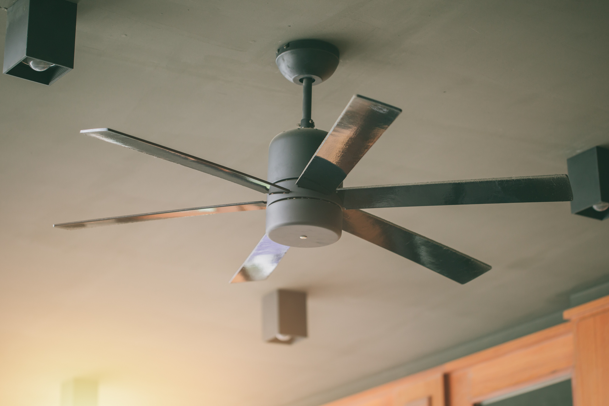 A modern ceiling fan with five blades is mounted on the ceiling, surrounded by recessed lighting.