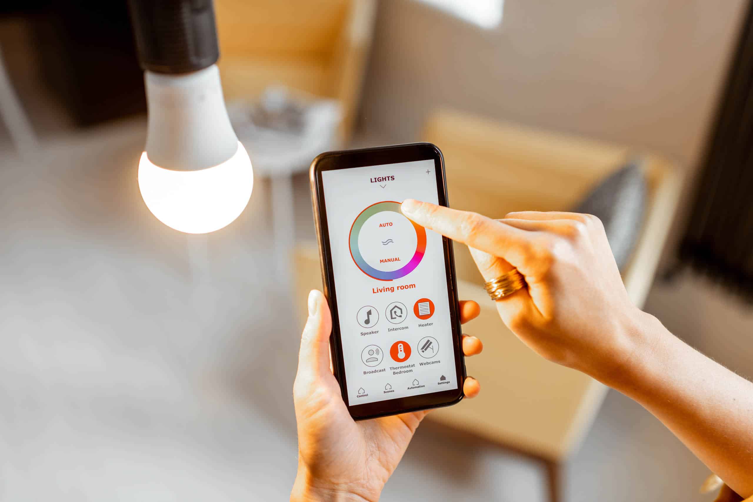 Person using a smartphone app to control a living room light. The interface shows brightness and on/off options.