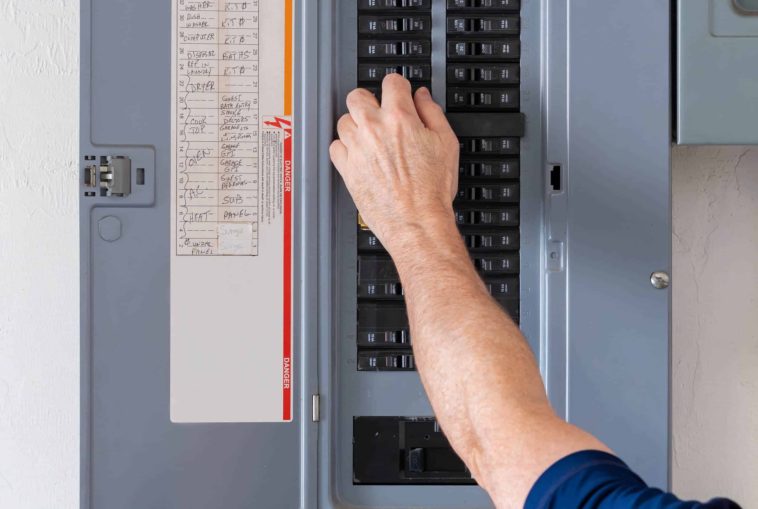 A person adjusts a breaker switch in an open electrical panel.