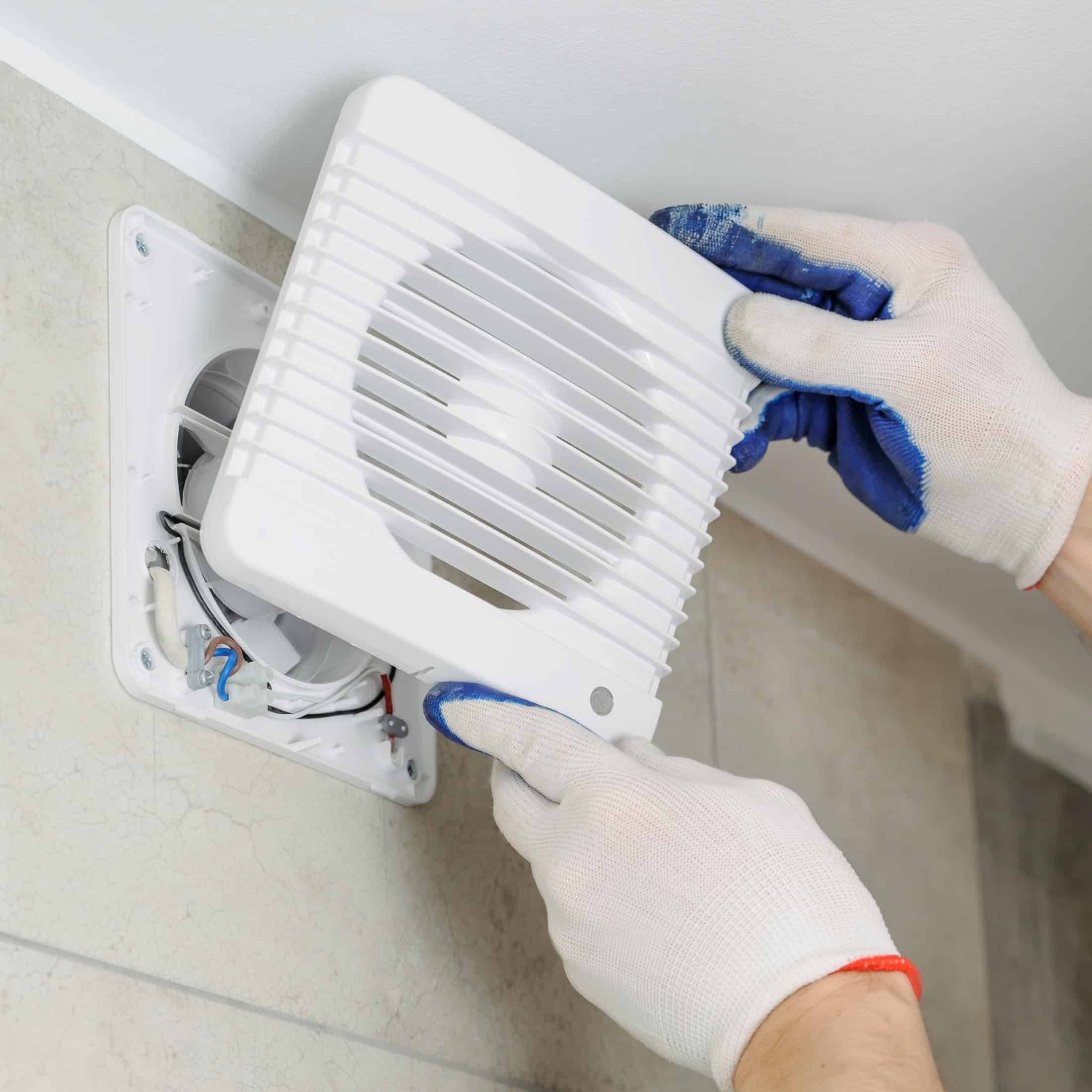 Person wearing gloves installs a white vent cover on a wall.