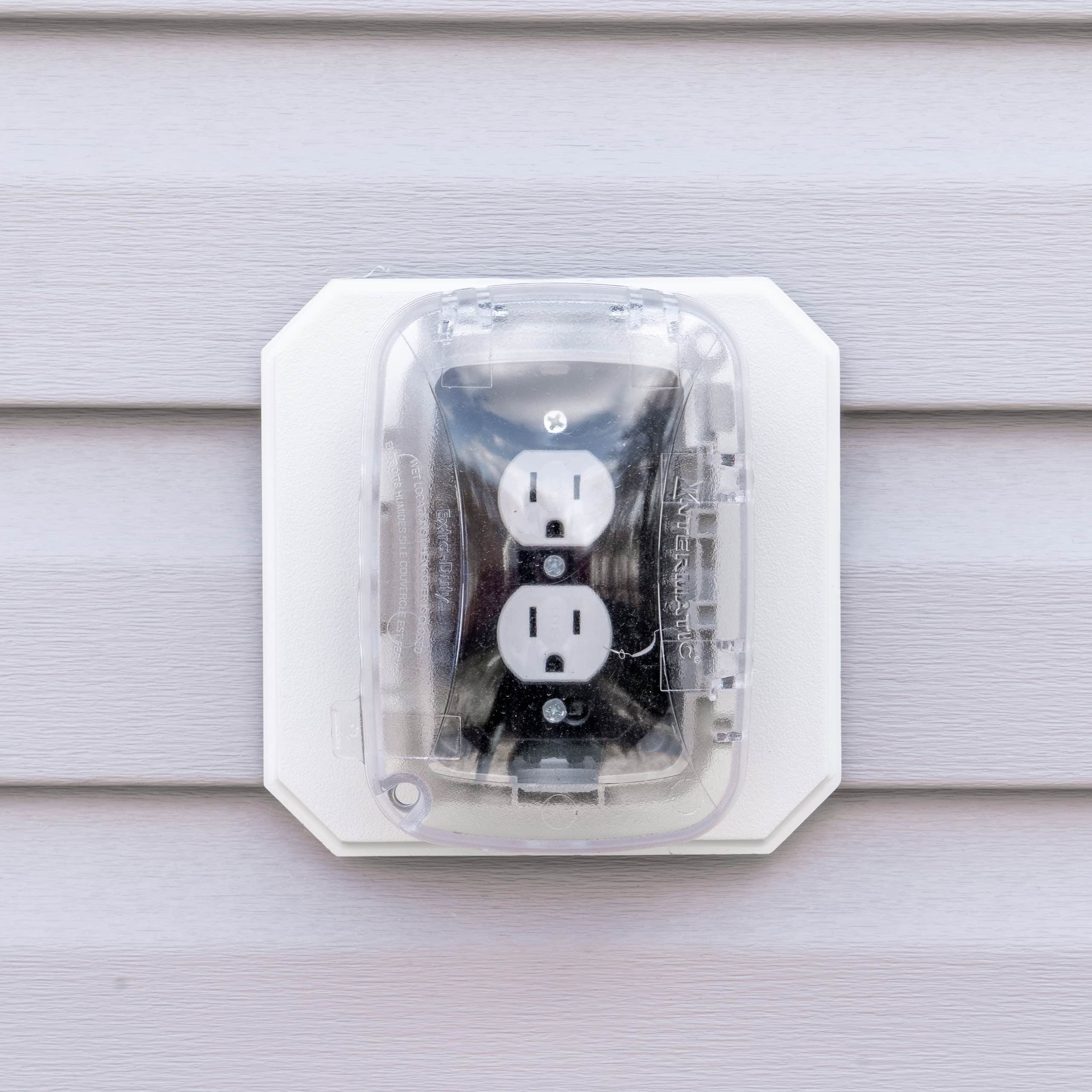 Outdoor electrical outlet with cover mounted on a vinyl siding wall.