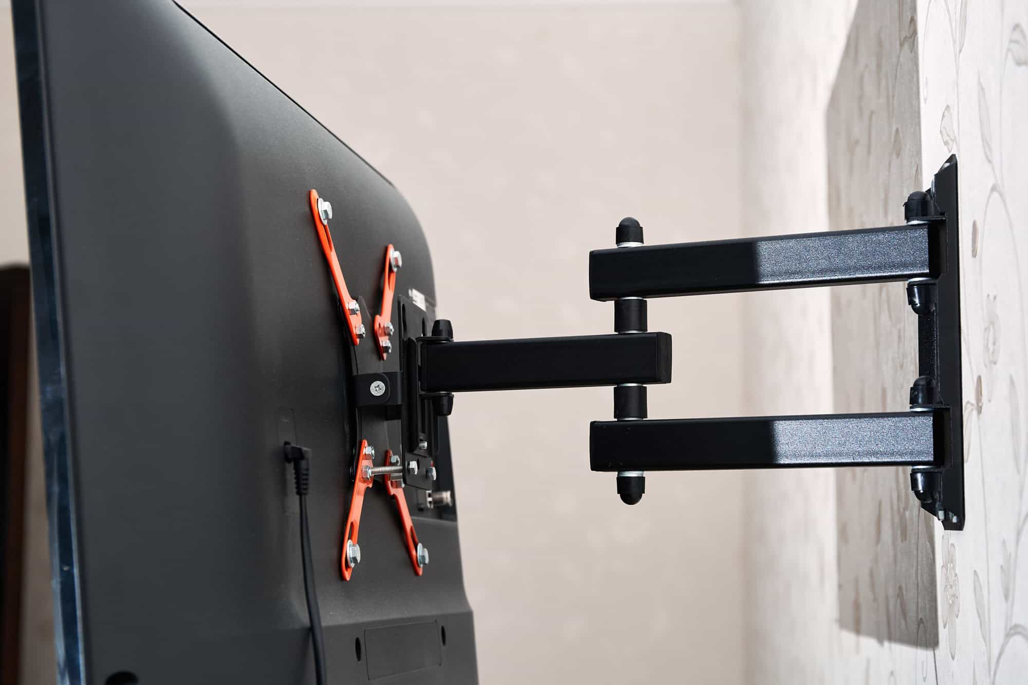 Back view of a wall-mounted flat-screen TV with an adjustable black and orange bracket.