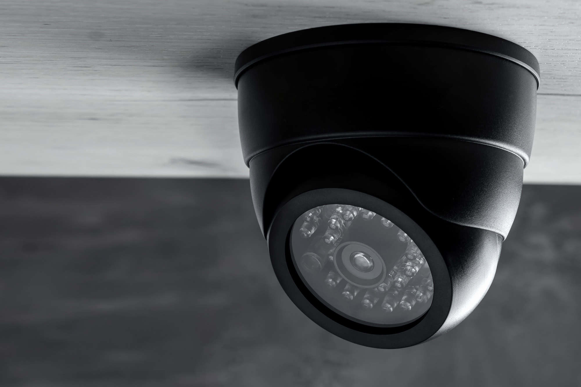 A home security camera attached to the ceiling of a house outside.