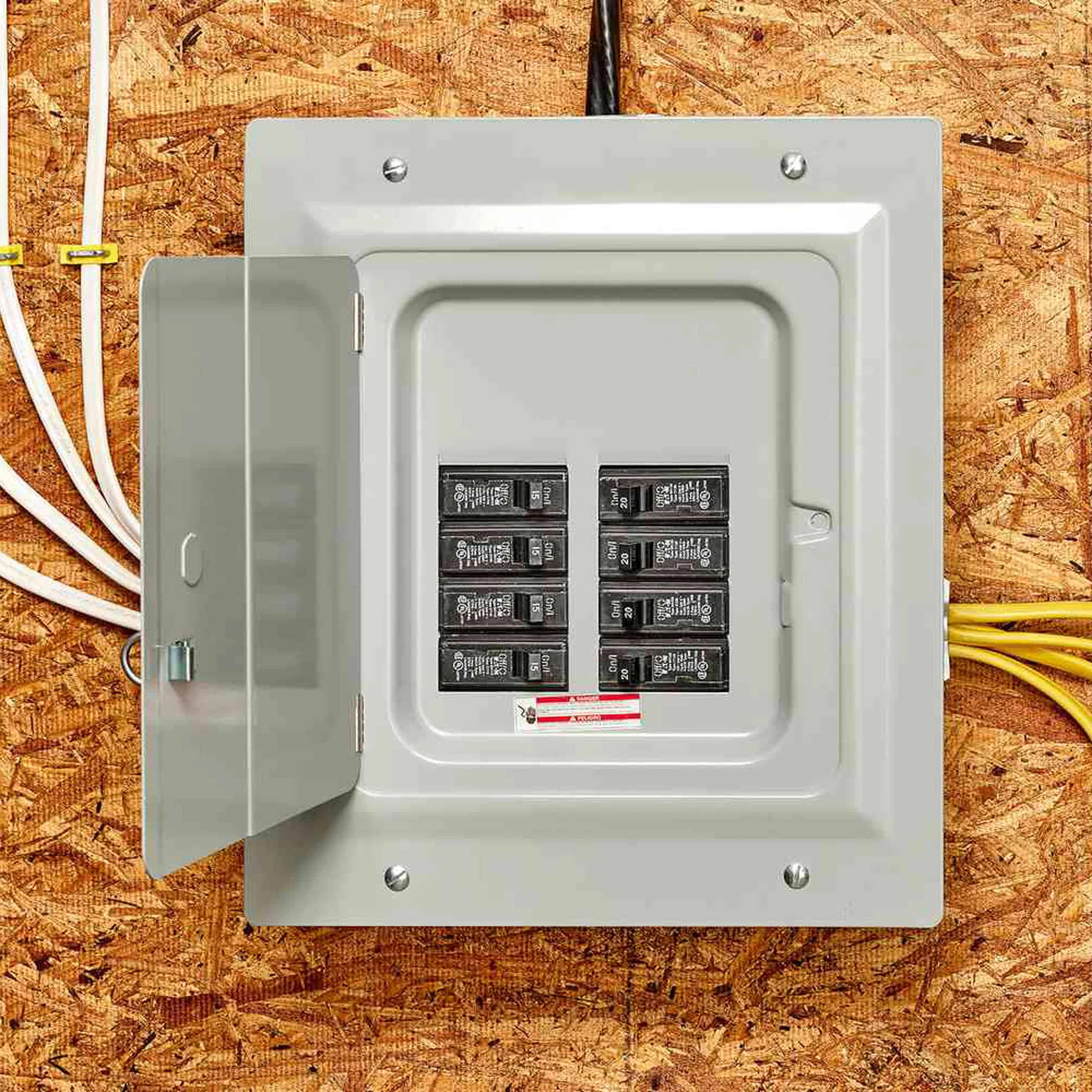 An open electrical panel with circuit breakers mounted on a plywood wall, showing wires entering from the top and right side.